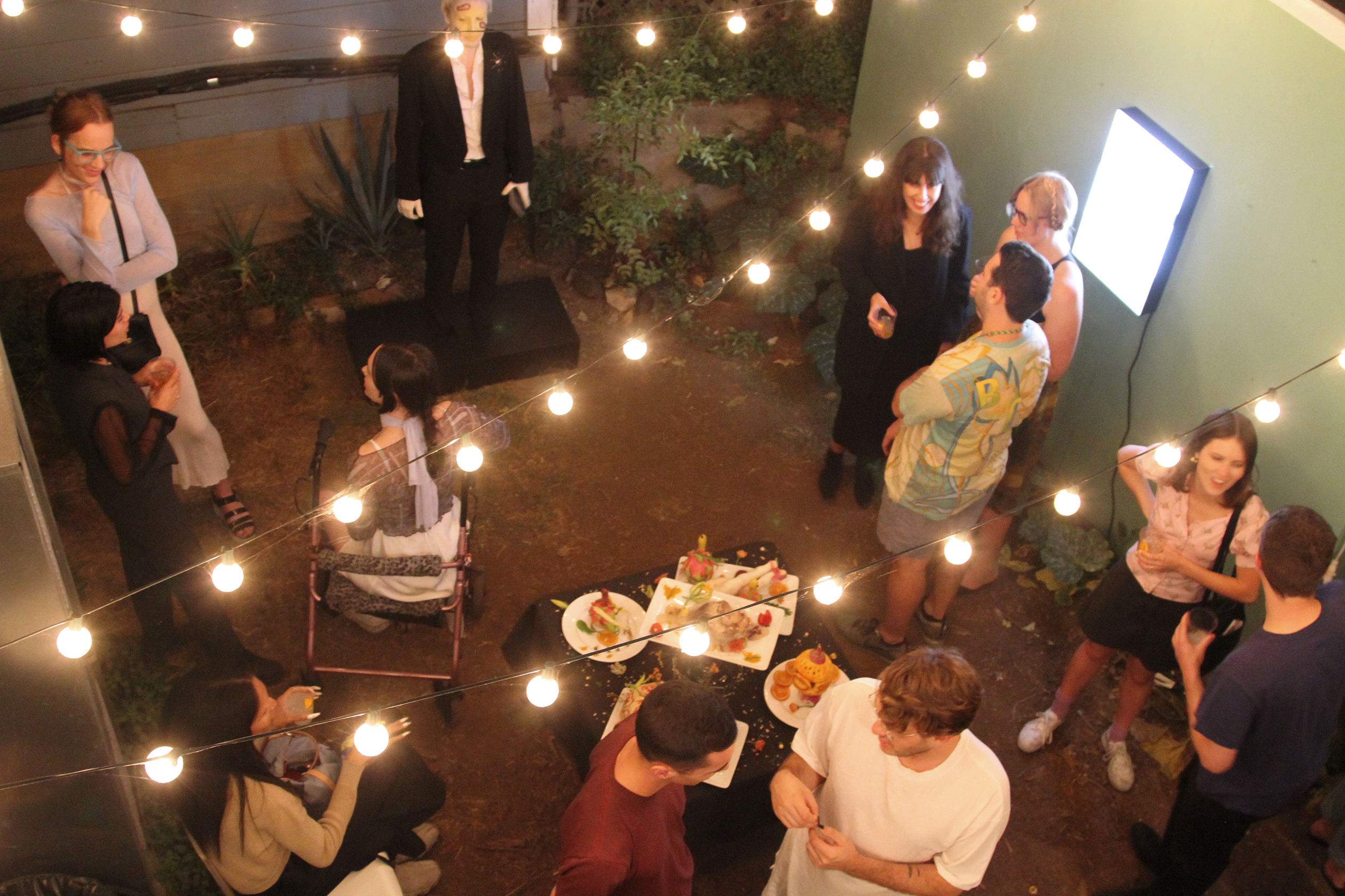 Birds eye shot of people in a backyard at night socializing with string lights in the foreground